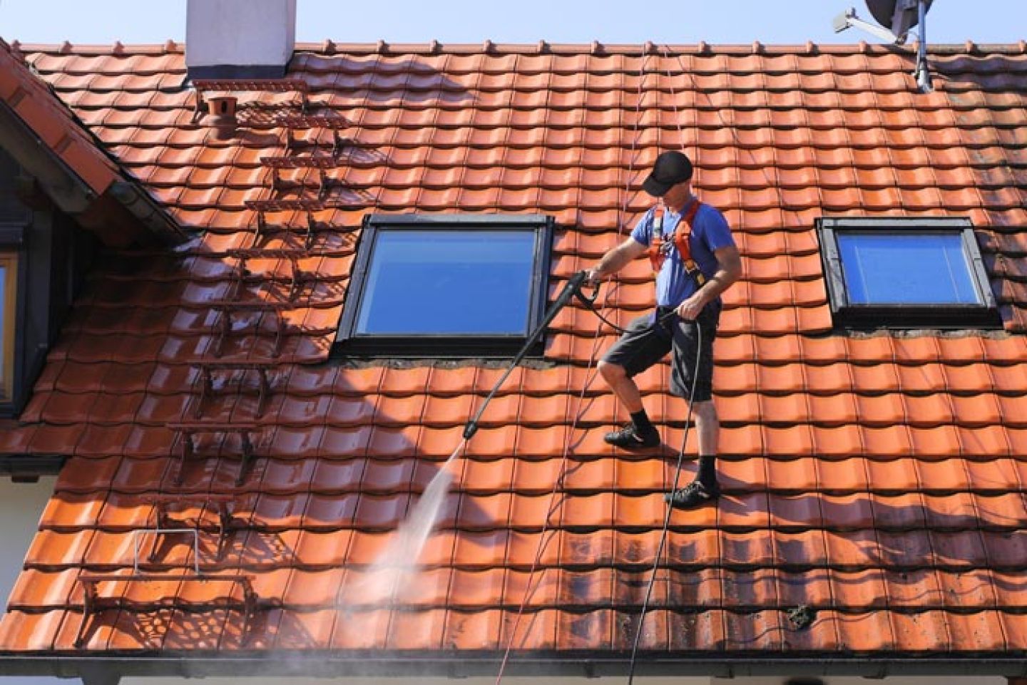 Man met valbeveiliging aan het werk op een dak met de hogedrukspuit