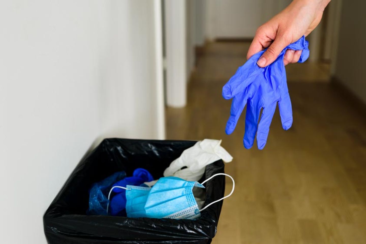 Vrouw gooit blauwe disposable werkhandschoenen in de vuilnisbak