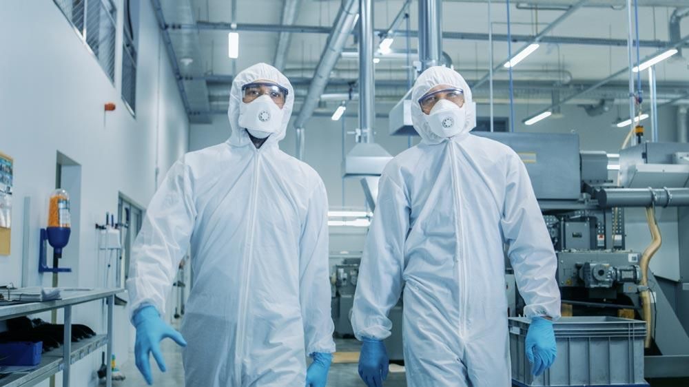 Twee mannen dragen een chemisch bestendige overall en lopen in een lab