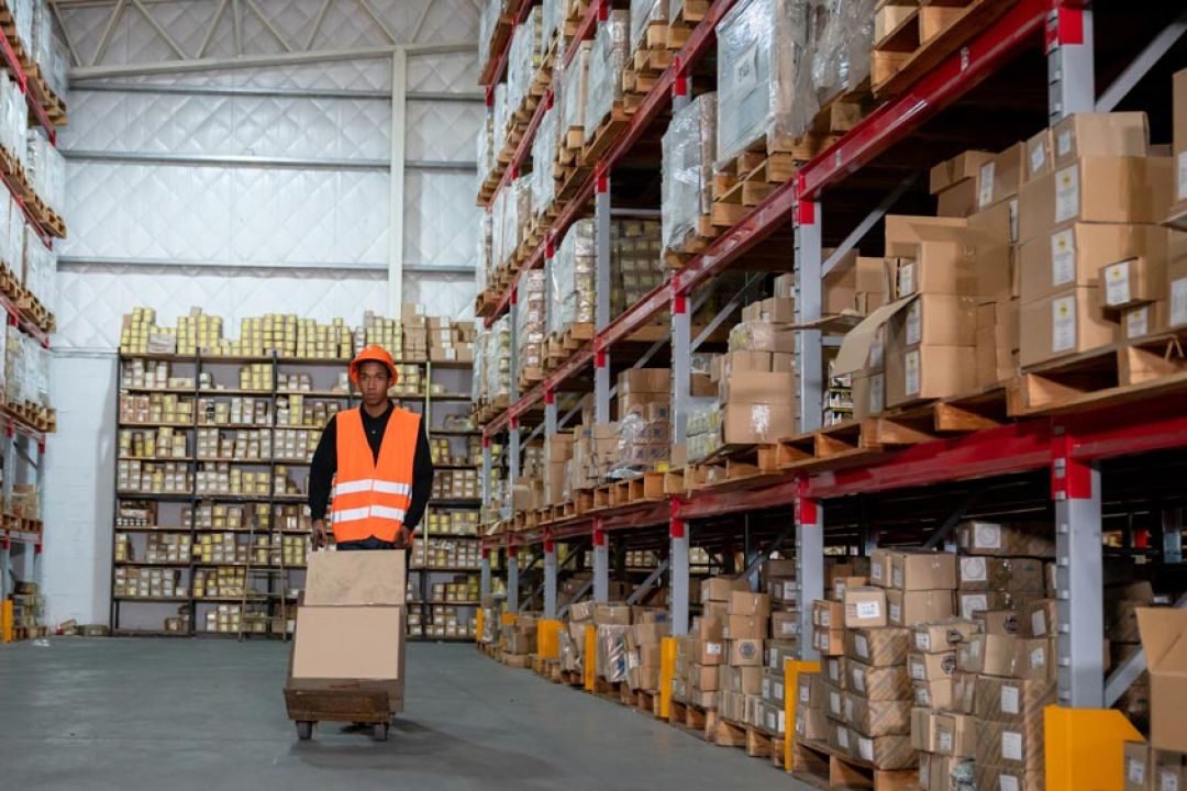 Man met oranje veiligheidshelm en -vestje verplaatst dozen in magazijn
