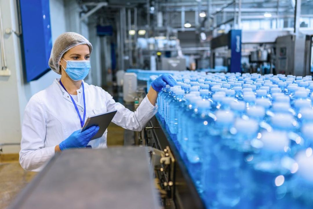 Vrouw met PBM voor de voedingsindustrie keurt blauwe flesjes in fabriek