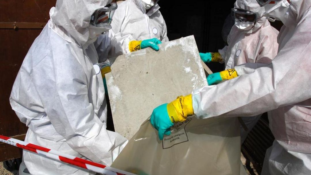 Vier mensen dragen persoonlijke beschermingsmiddelen, waaronder adembescherming, tijdens asbestsanering