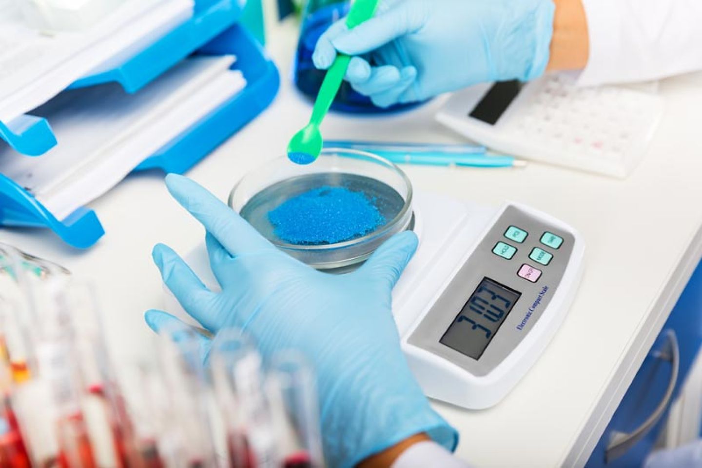 Vrouw draagt blauwe disposable handschoenen en weegt materiaal af in een lab