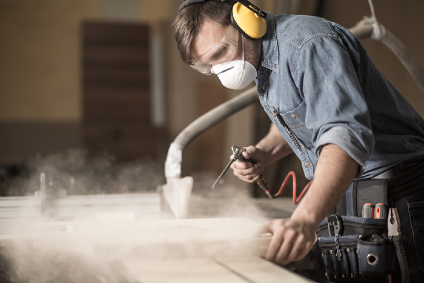 Man draagt een stofmasker, veiligheidsbril en gehoorkap tijdens het werken om zichzelf te beschermen