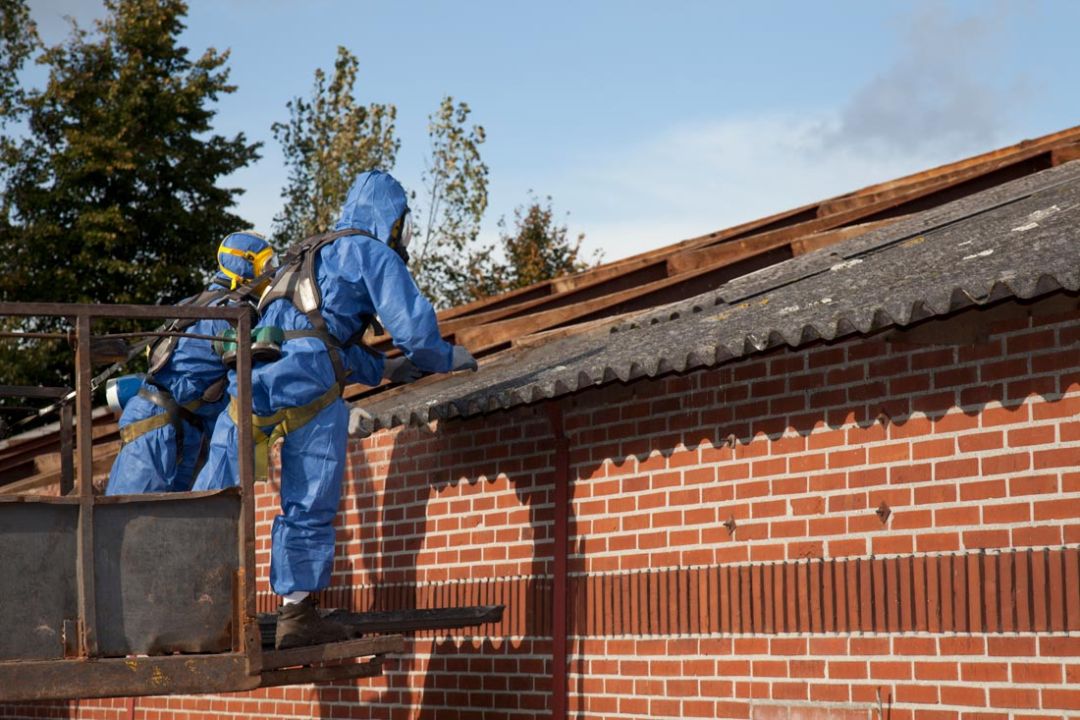 Twee mannen dragen persoonlijke beschermingsmiddelen tijdens asbestsanering op een dak